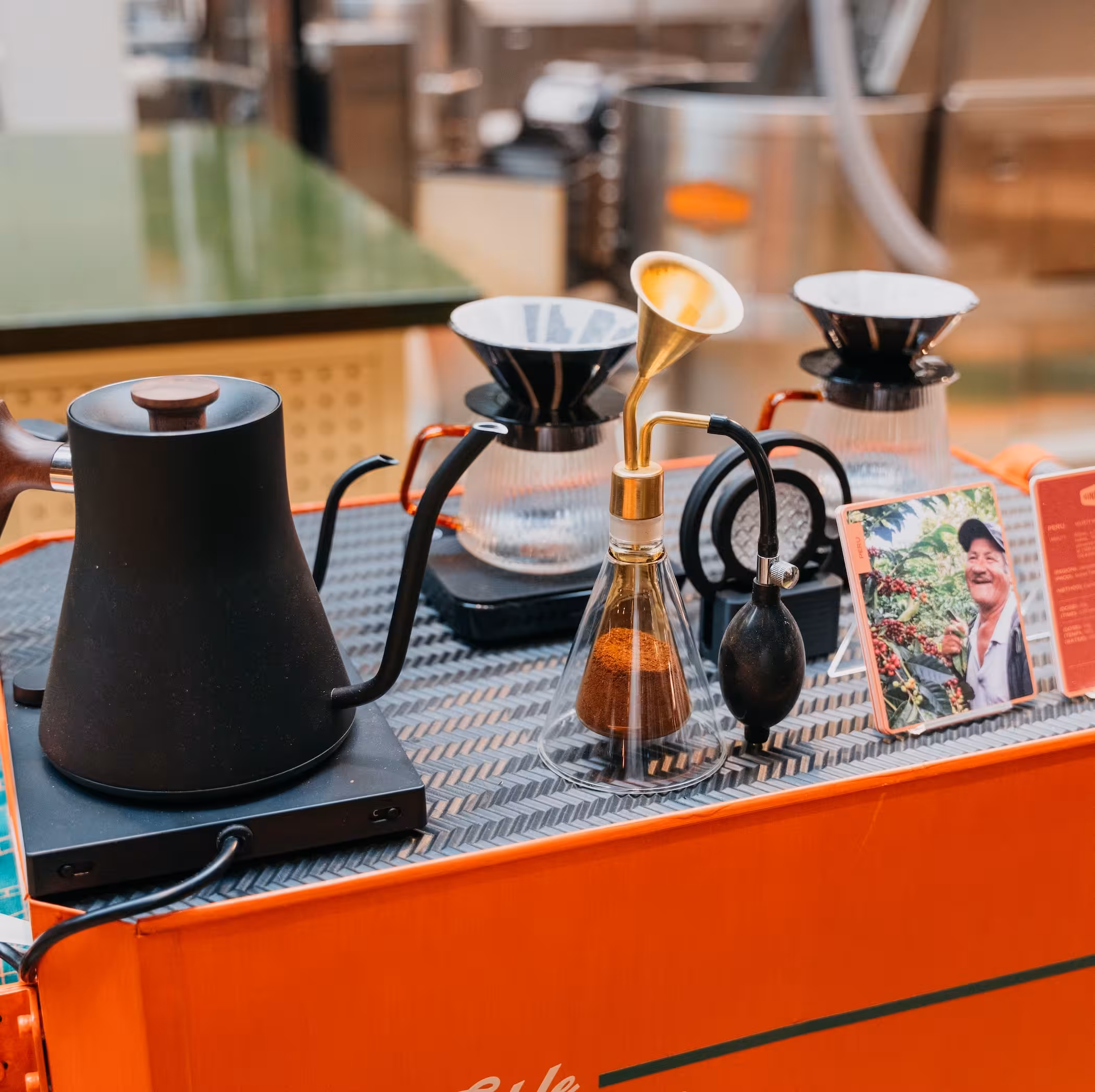 Close up of bright orange cart, with a black kettle, two pour over drip coffee filters and glasses, and a coffee aroma diffuser