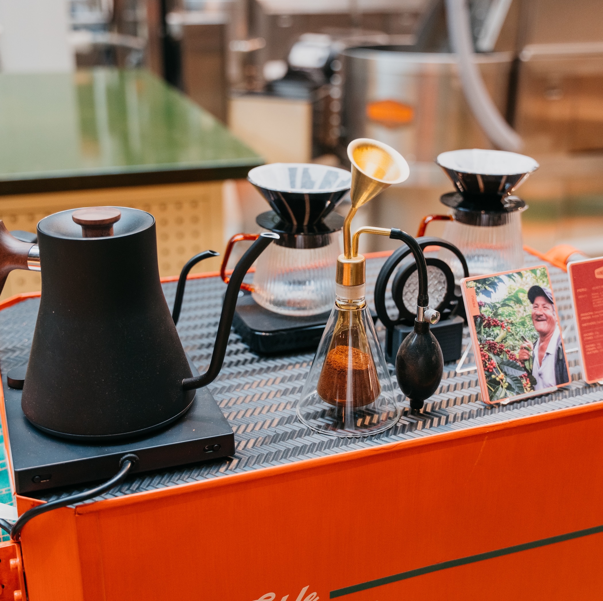 Close up of bright orange cart, with a black kettle, two pour over drip coffee filters and glasses, and a coffee aroma diffuser